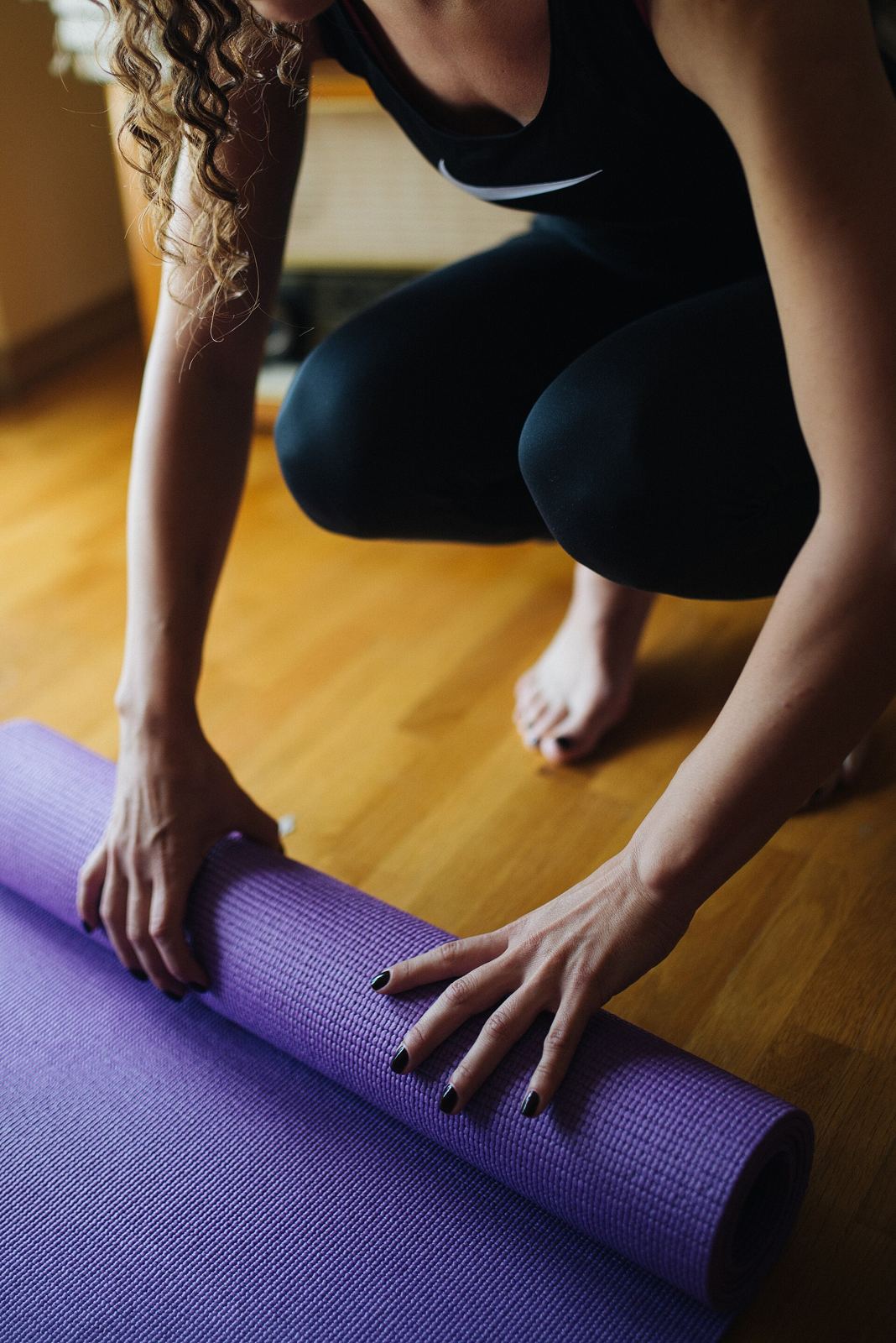Hands unrolling a purple mat across a warm wooden studio floor
